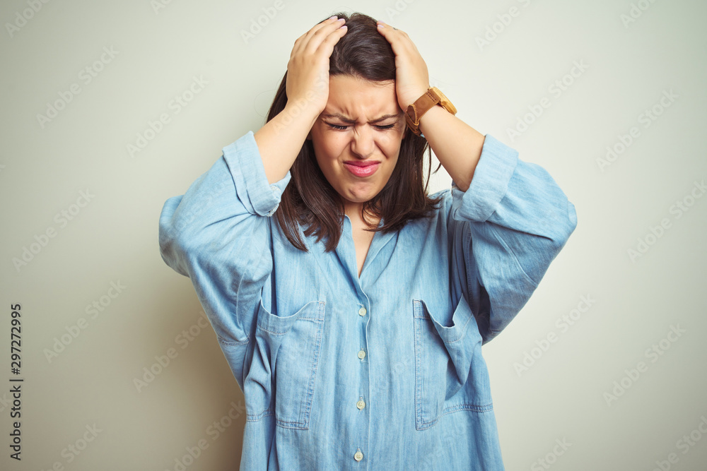Young beautiful brunette woman wearing casual blue denim shirt over isolated background suffering from headache desperate and stressed because pain and migraine. Hands on head.