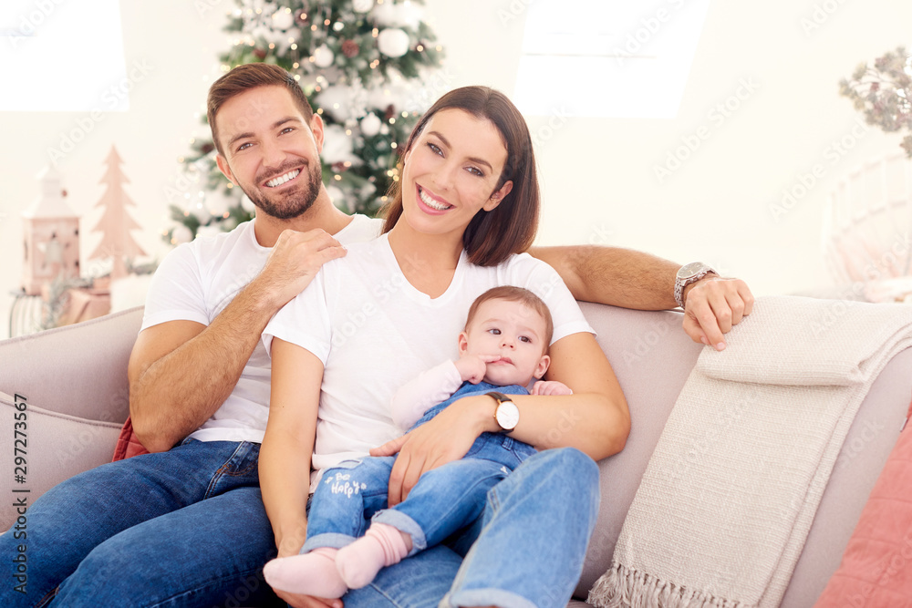 Lovely family with their baby girl relaxing on sofa at home during Christmas Lovely family with their baby girl relaxing on sofa at home during Christmas