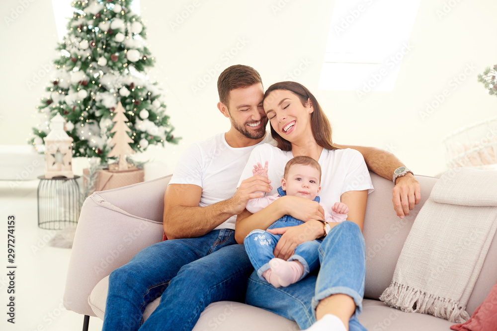 Lovely family with their baby girl relaxing on sofa at home during Christmas Lovely family with their baby girl relaxing on sofa at home during Christmas