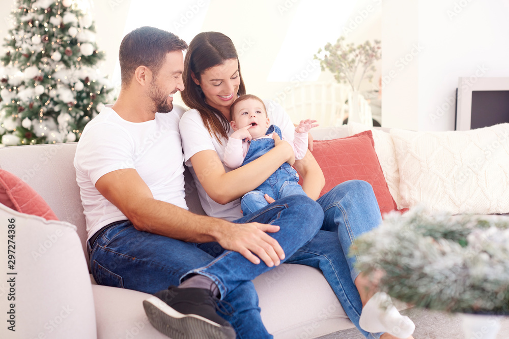 Lovely family with their baby girl relaxing on sofa at home during Christmas