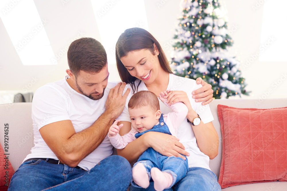 Lovely family with their baby girl relaxing on sofa at home during Christmas