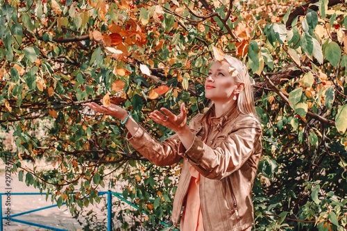 Young beautiful blonde woman throwing up fallen autumn leaves over her head standing on the ground in the park.