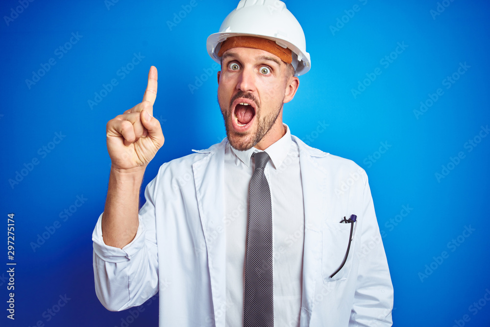 Young handsome engineer man wearing safety helmet over blue isolated background pointing finger up with successful idea. Exited and happy. Number one.