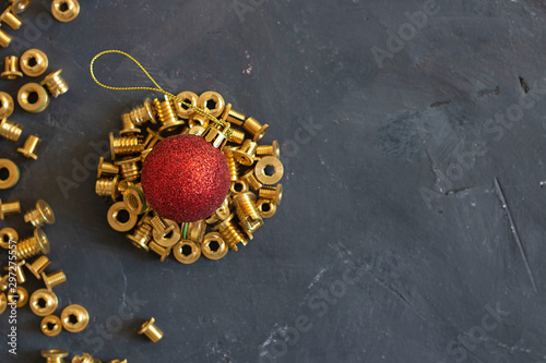 Round form made of gold pop rivet nuts ond lochnuts with red christmas ball on it on black tectured chalk board. Horizontal copy space. Fasteners, screws and details. Top view. New year concept.