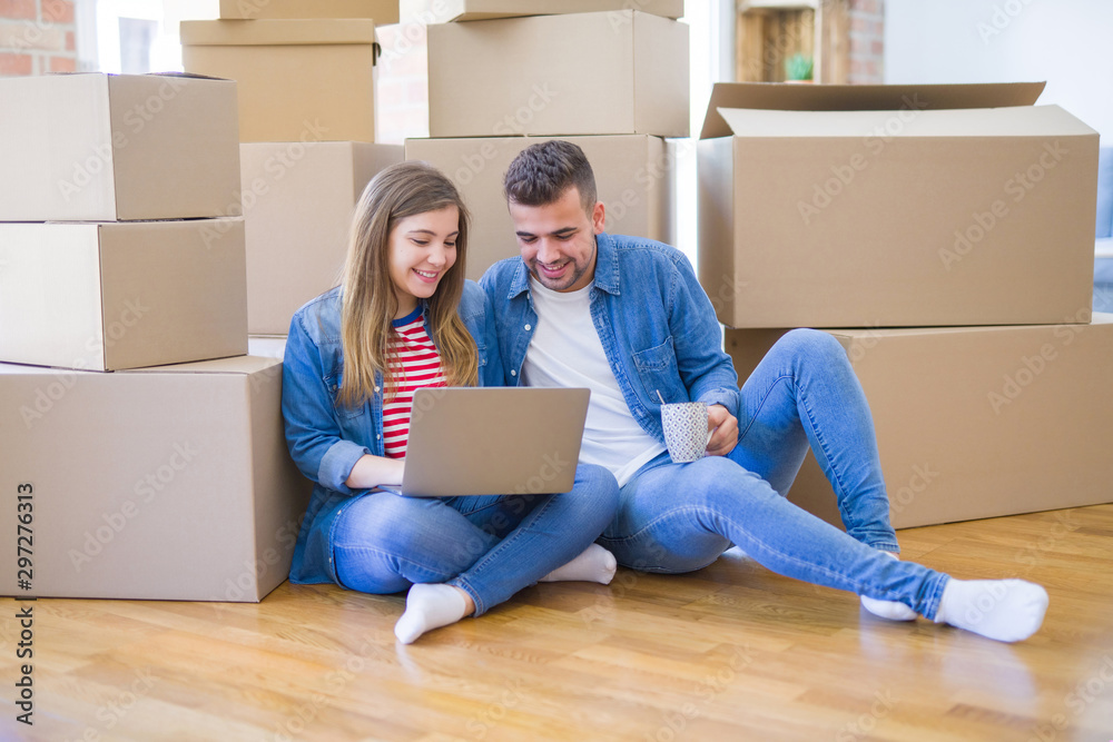 Young couple sitting on the floor around cardboard boxes using computer laptop, very happy moving to a new house Young couple sitting on the floor around cardboard boxes using computer laptop, very happy moving to a new house