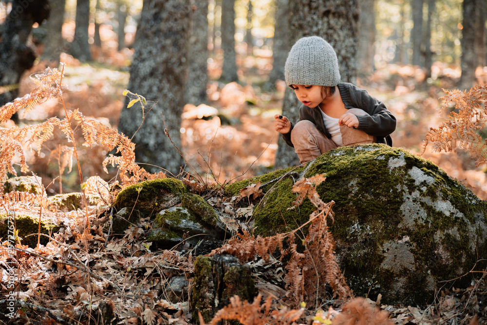 Little caucasian baby girl squatting in the forest among ferns