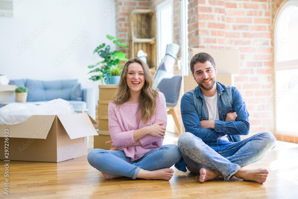 Young beautiful couple moving to a new house sitting on the floor happy face smiling with crossed arms looking at the camera. Positive person. Young beautiful couple moving to a new house sitting on the floor happy face smiling with crossed arms looking at the camera. Positive person.