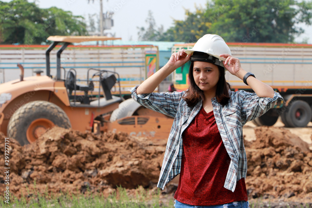 Obraz premium Female civil engineer standing and catch the white helmet on loader pedal car and pile of soil background.
