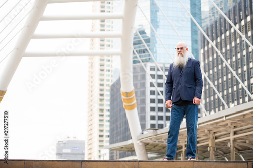 Full body shot of mature bearded bald businessman in the city outdoors