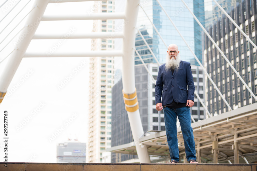 Full body shot of mature bearded bald businessman in the city outdoors