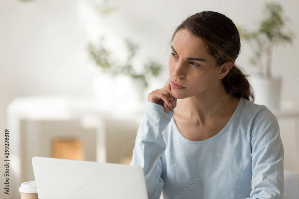 Thoughtful millennial woman sitting with computer at workplace, looking aside. Thoughtful millennial woman sitting with computer at workplace, looking aside.