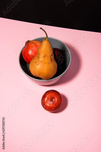 Autumn seasonal fruits on pink table with black background. Pomegranate, pear and plum. Abstract conception.
