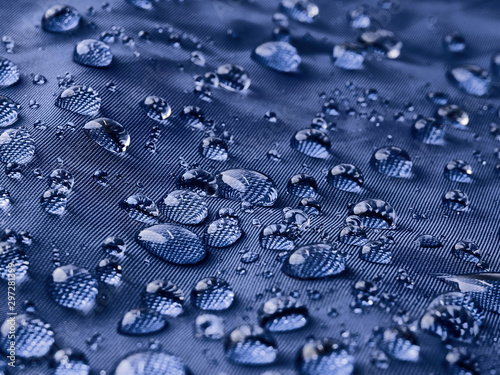 Rain water droplets on blue fiber waterproof fabric. Blue background.
