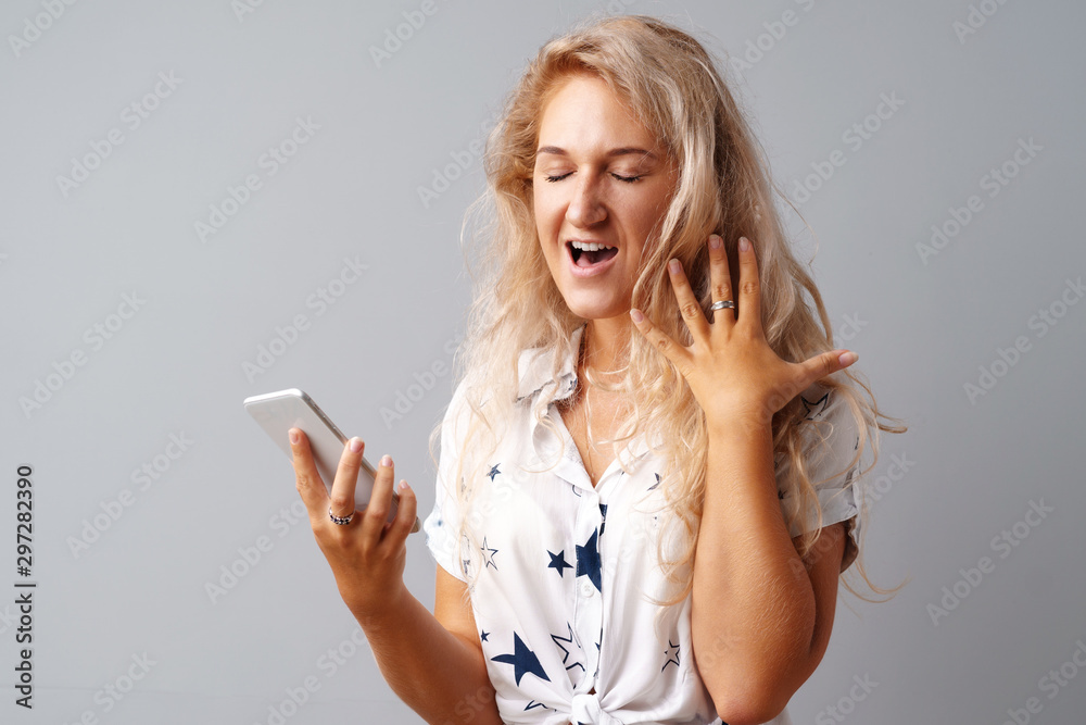 Blonde young casual woman looking at her phone over gray background. Blonde young casual woman looking at her phone over gray background.