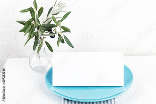 minimalistic composition with cards mock up for invitation, menu, place card on a pastel blue porcelain plate with olive branch on white background
