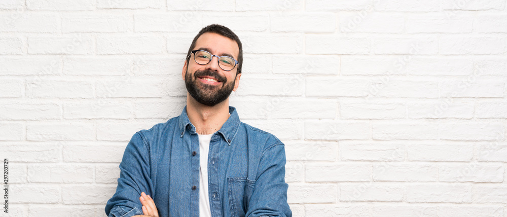 Handsome man with beard over white brick wall with glasses and happy - obrazy, fototapety, plakaty 