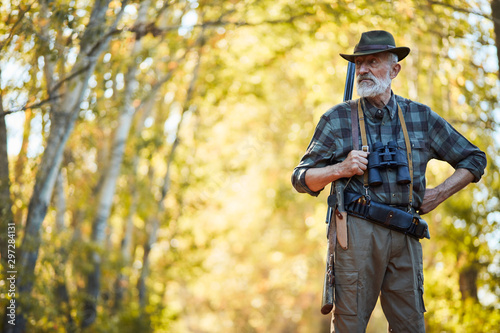 Bearded caucasian hunter wearing cowboy hat in search of trophy in autumn forest. Stand looking for prey in hunting period, autumn season open.
