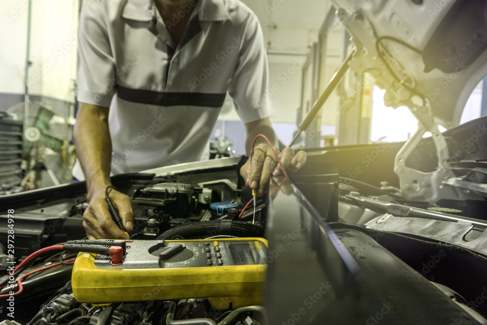 Auto mechanic using multimeter with probe to checking wiring circuit in car in garage. Repair service.	