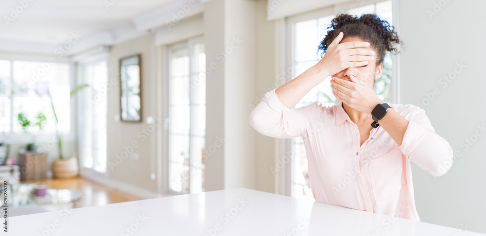 Wide angle of beautiful african american woman with afro hair Covering eyes and mouth with hands, surprised and shocked. Hiding emotion Wide angle of beautiful african american woman with afro hair Covering eyes and mouth with hands, surprised and shocked. Hiding emotion