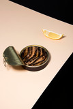 Opened oily fish, sardine tin with lemon on powder tabletop and black background. Abstract food conception.