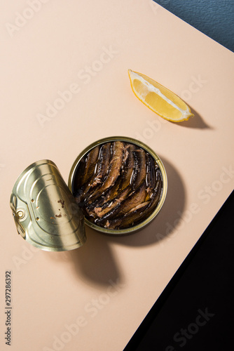 Opened oily fish, sardine tin with lemon on powder tabletop and black background. Abstract food conception.