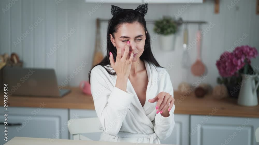 Young woman in bathrobe applies cream on her face and does facial massage Young woman in bathrobe applies cream on her face and does facial massage
