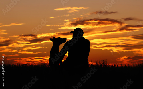A man and a dog against the background of an incredible sunset, a beautiful sunset, a man and a Belgian shepherd dog Malinois admire the sunset, look into the distance, sit together