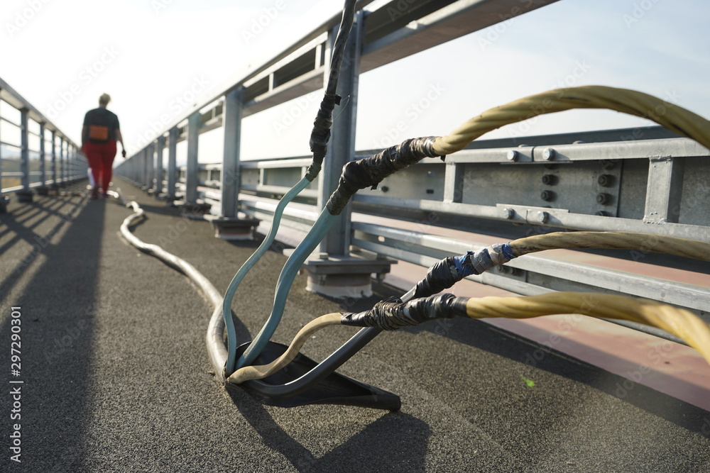 Power electric cable on the bridge. Power cable on the pedestrian area of the road. A man walking by an electric cable. Power electric cable on the bridge. Power cable on the pedestrian area of the road. A man walking by an electric cable.