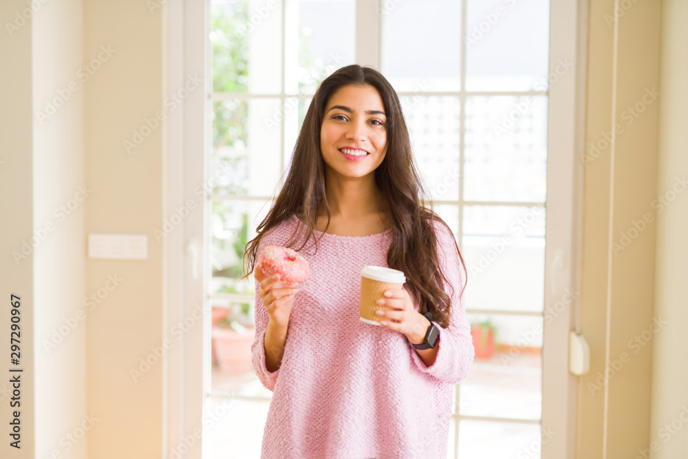Young worker woman taking a break eating tasty pink donut and drinking a cup of coffee Young worker woman taking a break eating tasty pink donut and drinking a cup of coffee