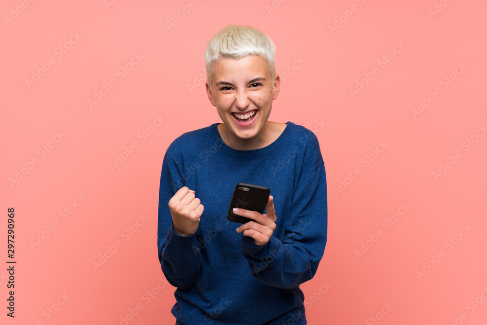 Teenager girl with white short hair over pink wall with phone in victory position Teenager girl with white short hair over pink wall with phone in victory position