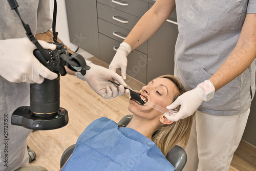 Dental doctor with blue mask checks the health of the mouth of his female patient lying in the armchair of a modern dental clinic. Photographing with a reflex the patient's teeth. Macro photography © JavierBallesterLegua