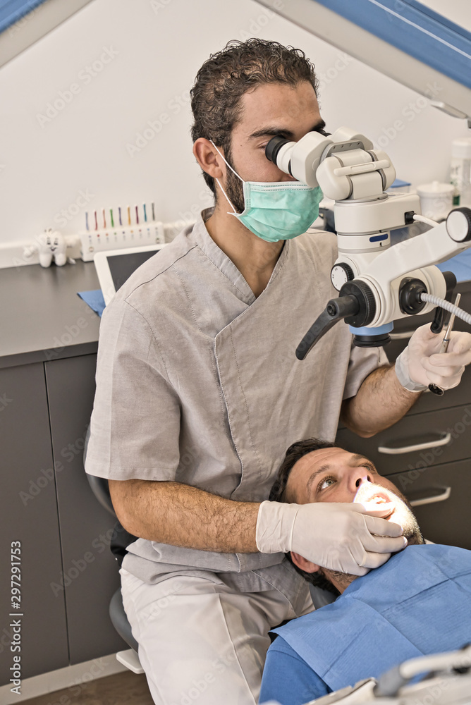 Dental doctor with microscope and hygienic gloves checking the dental health of his patient in a modern clinic Dental doctor with microscope and hygienic gloves checking the dental health of his patient in a modern clinic