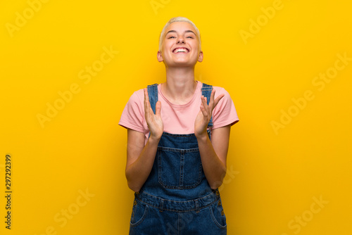 Teenager girl with overalls on yellow background applauding after presentation in a conference