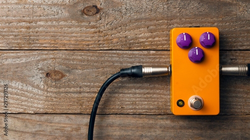 Blank orange guitar pedal with purple knobs and plugged jacks on wooden floor