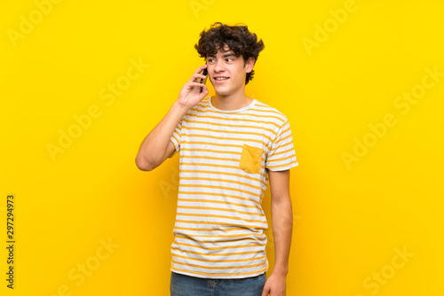Young man over isolated yellow wall keeping a conversation with the mobile phone