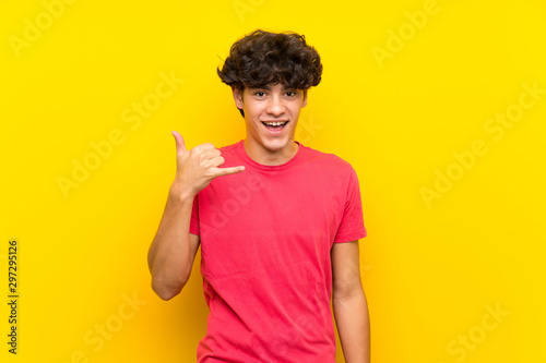 Young man over isolated yellow wall making phone gesture