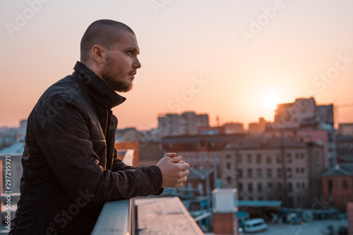 young handsome serious man looks away on the background of the city at sunset
