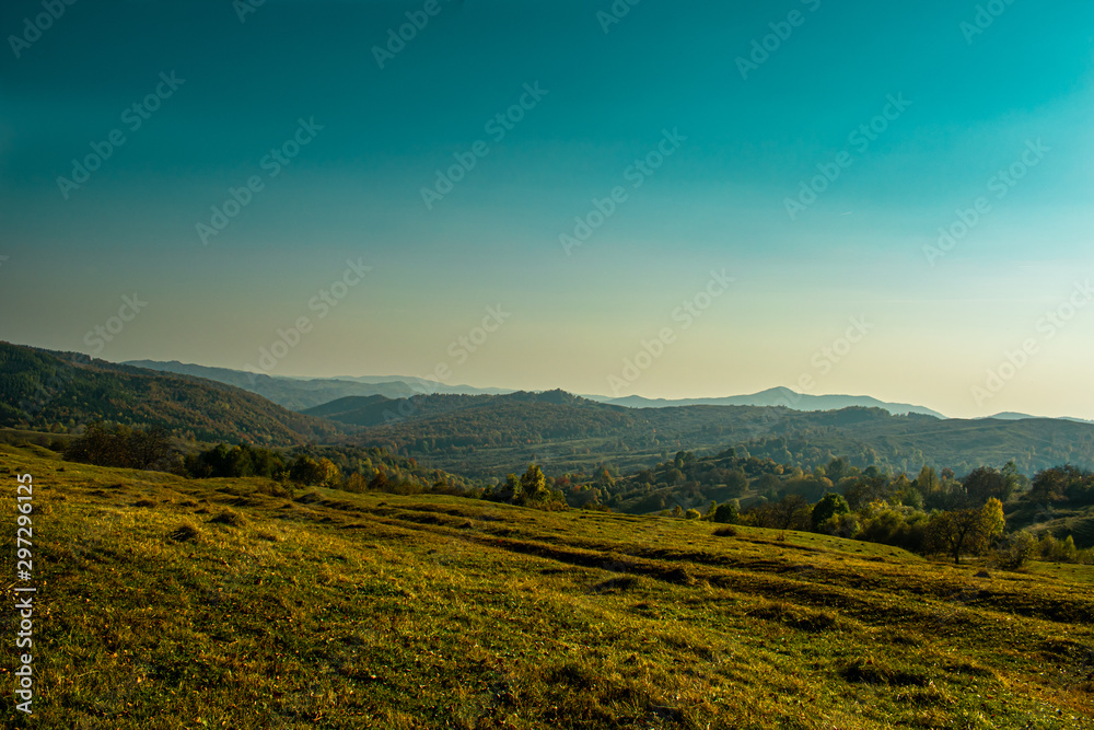 Evening sunshine on a beautiful hill near a small village, with few trees and autumn colors