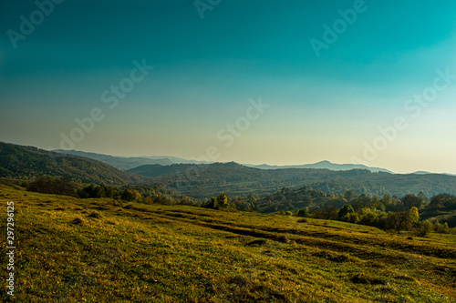 Evening sunshine on a beautiful hill near a small village  with few trees and autumn colors