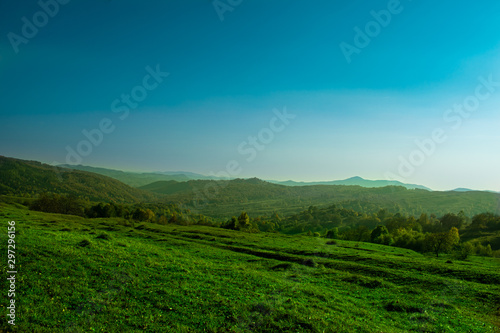 Evening sunshine on a beautiful hill near a small village, with few trees and autumn colors © Paraschiv