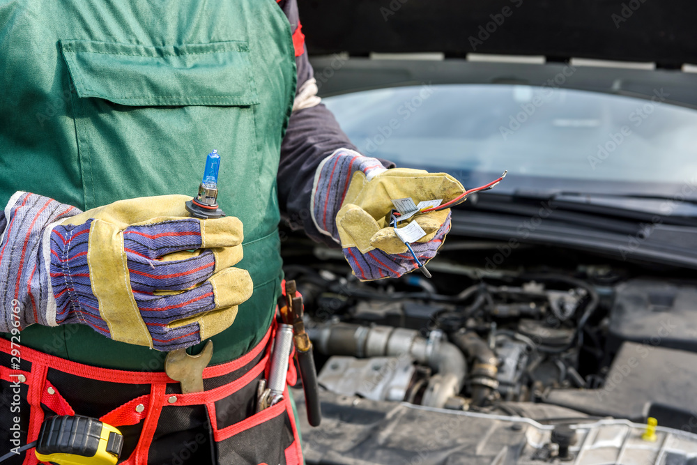 Mechanic holding lamp and cables from headlamp of car - obrazy, fototapety, plakaty 