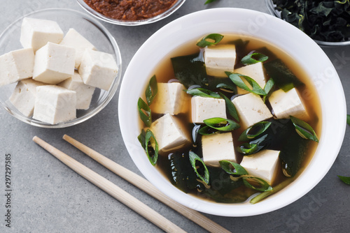 Bowl with miso soup, wakame seaweed, miso pasta, tofu and chopsticks on a gray background. photo