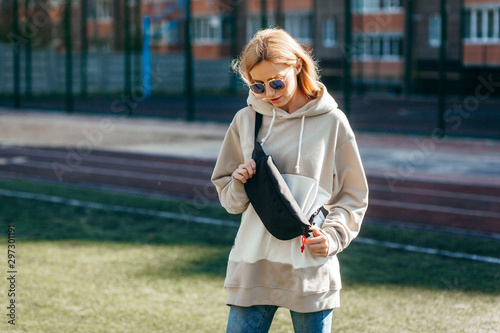 Stylish model girl at the city in a grey hoodie and glasses with waist bag