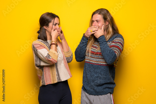 Hippie couple over yellow background covering mouth with hands for saying something inappropriate