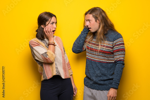 Hippie couple over yellow background surprised and shocked while looking right