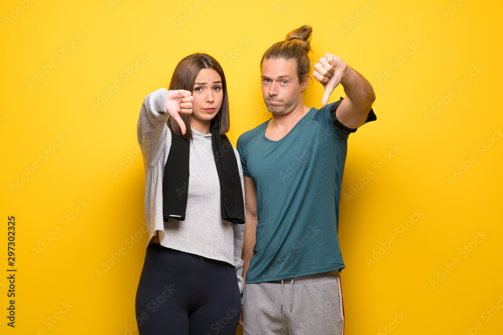 Fototapeta premium Grupa sportowców na żółtym tle pokazuje kciuk w dół znak z negatywnym wyrazem