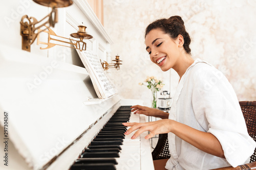 Lady in white shirt play the piano indoors at home.