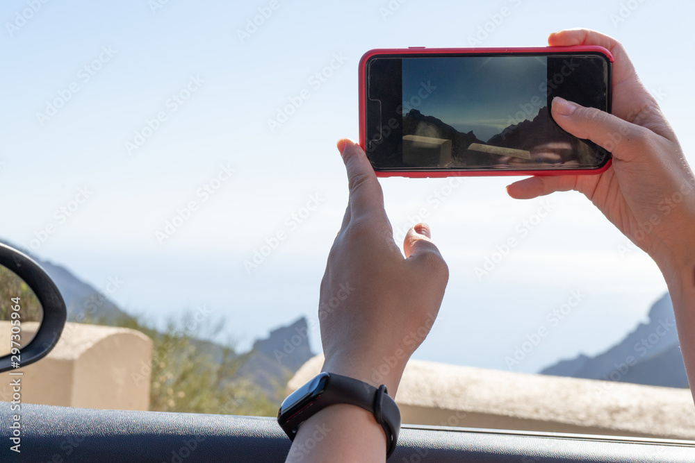 Tourist woman hand take a picture to share in social media pressing the smart phone inside the rent a car in a journey. Passenger sitting taking a video with the window down and drive.