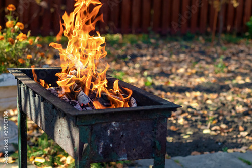 Portable metal grill with burning wood and red fire. Barbecue on the street. Fire and charcoal grilled. Barbecue equipment. BBQ picnic. Bonfire safety in the country.