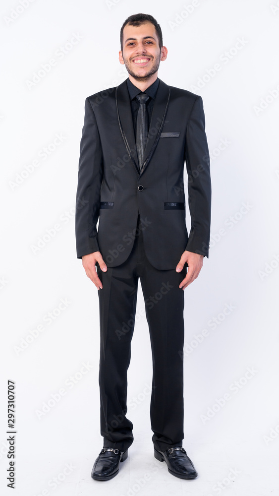 Full body shot of happy young bearded Persian businessman in suit smiling Full body shot of happy young bearded Persian businessman in suit smiling